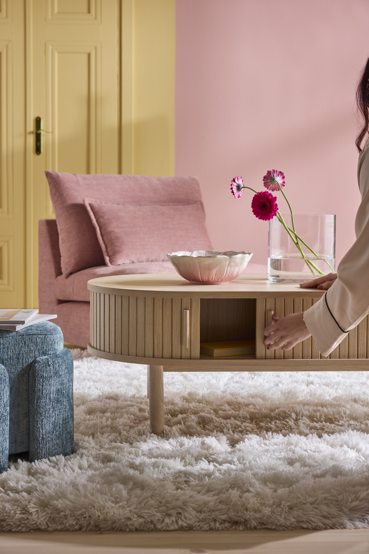 en vit ryamatta ligger på ett golv under ett träfärgat soffbord, en rosa soffa och blå puff