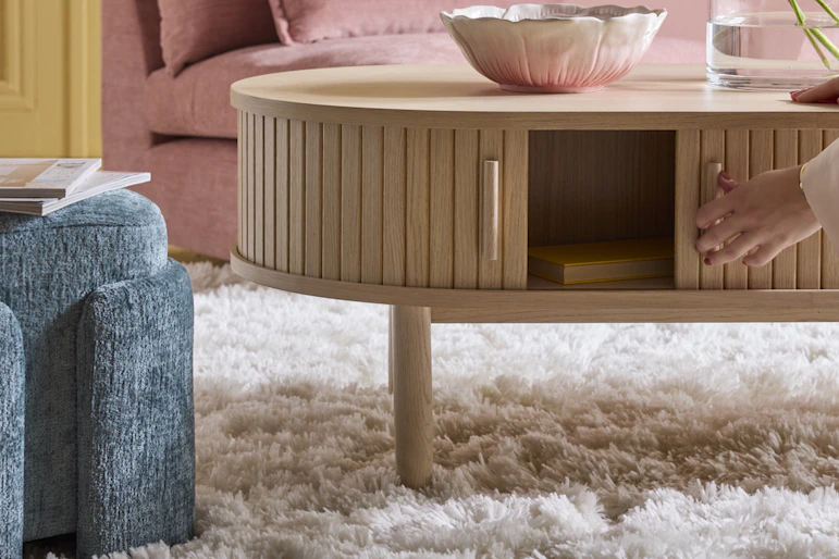 en vit ryamatta ligger på ett golv under ett träfärgat soffbord, en rosa soffa och blå puff