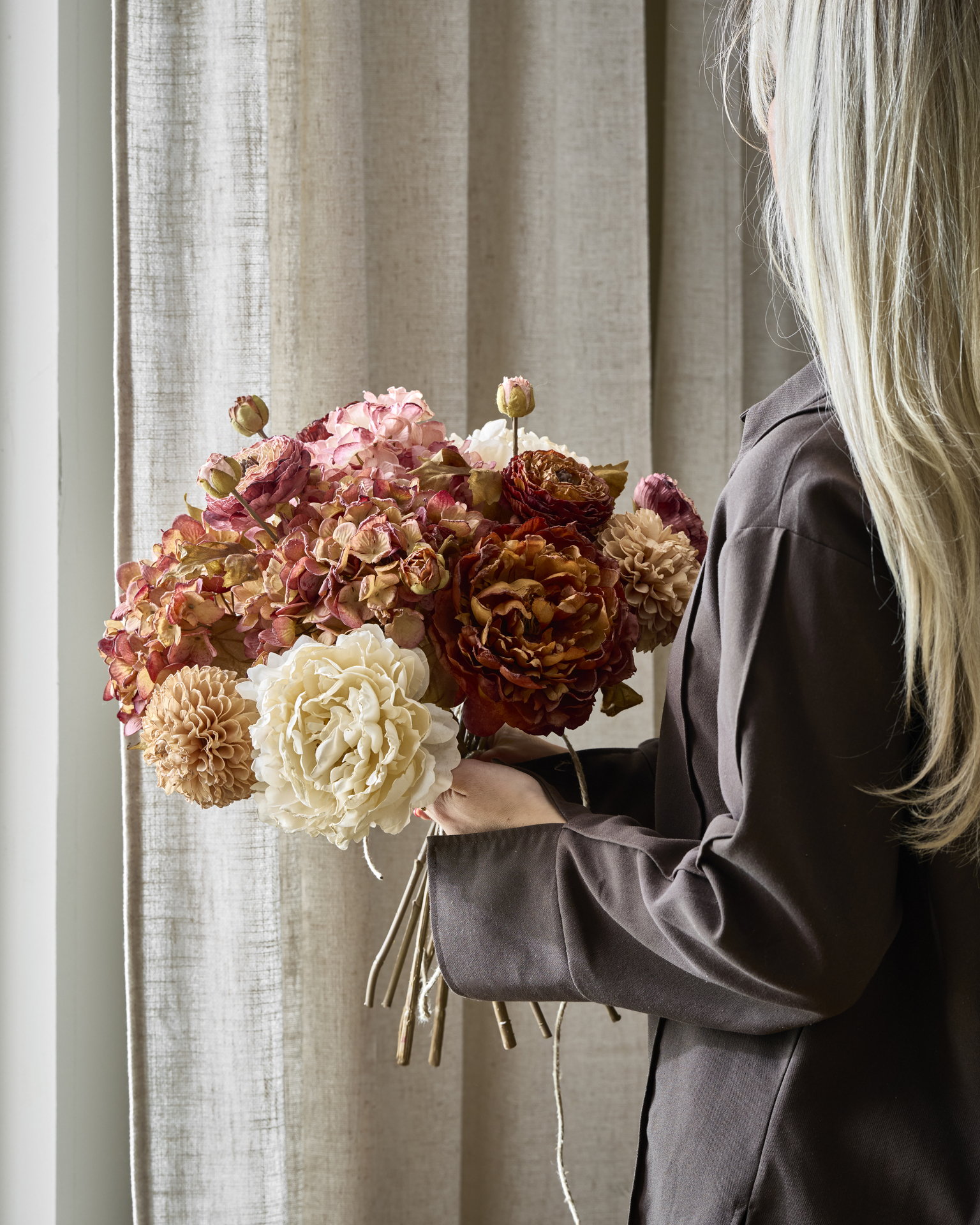en blond tjej håller i en bukett av konstväxter i dova färger