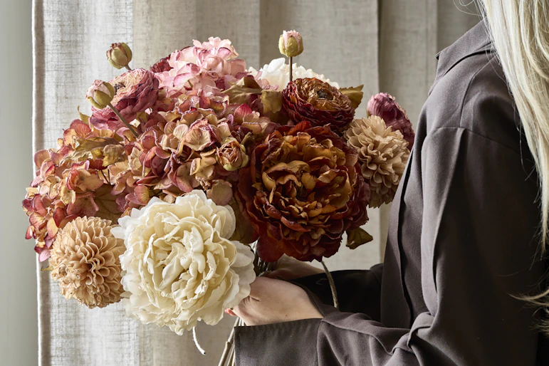 en blond tjej håller i en bukett av konstväxter i dova färger
