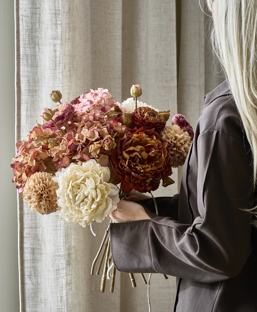 en blond tjej håller i en bukett av konstväxter i dova färger