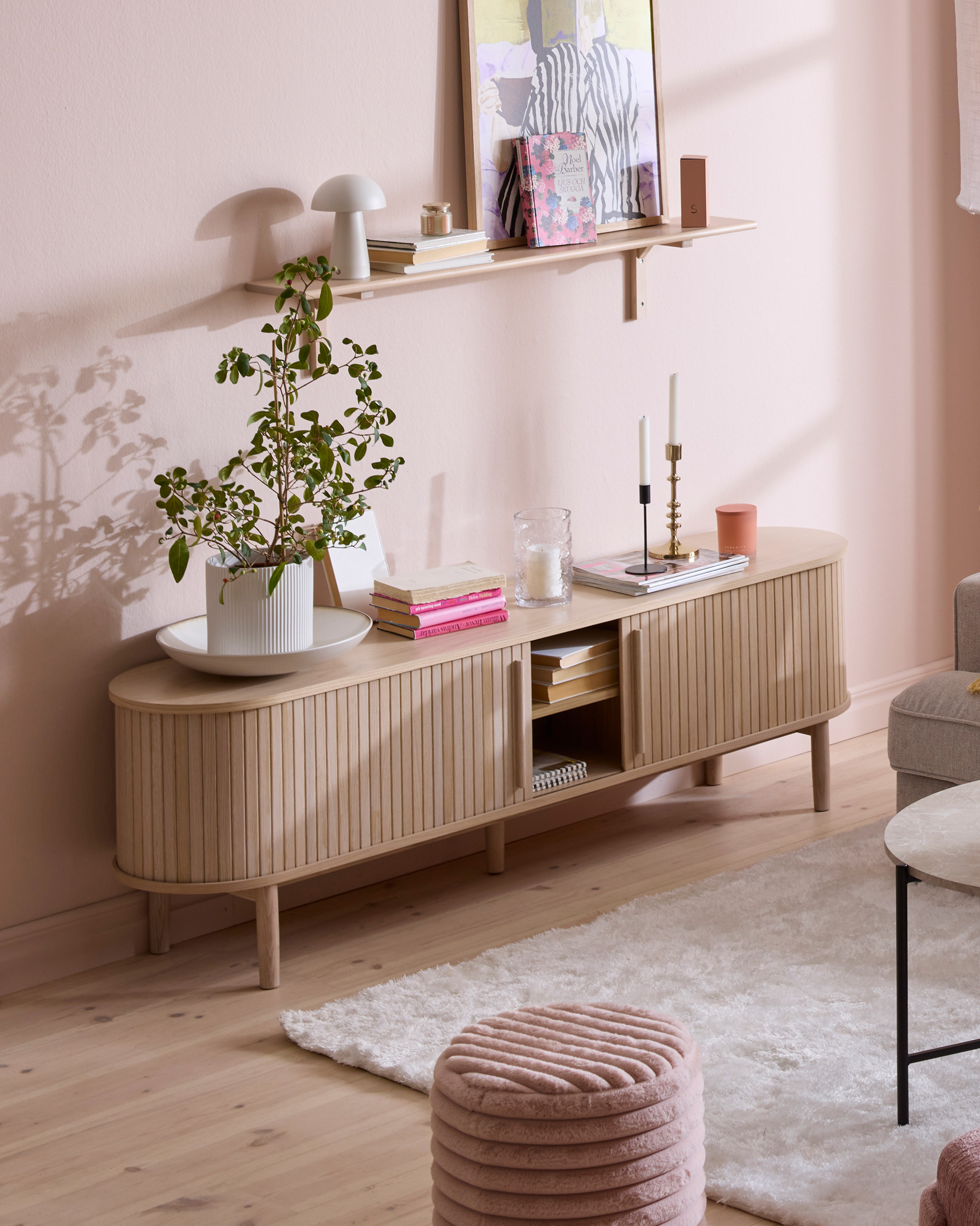 en tv-bänk i ljust trä med ribbor står i ett rum med rosa väggar