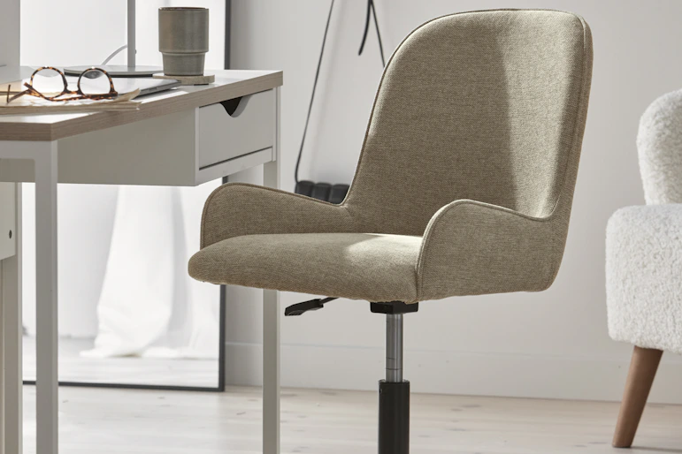 en beige skrivbordsstol står i ett ljust rum framför ett vitt skrivbord