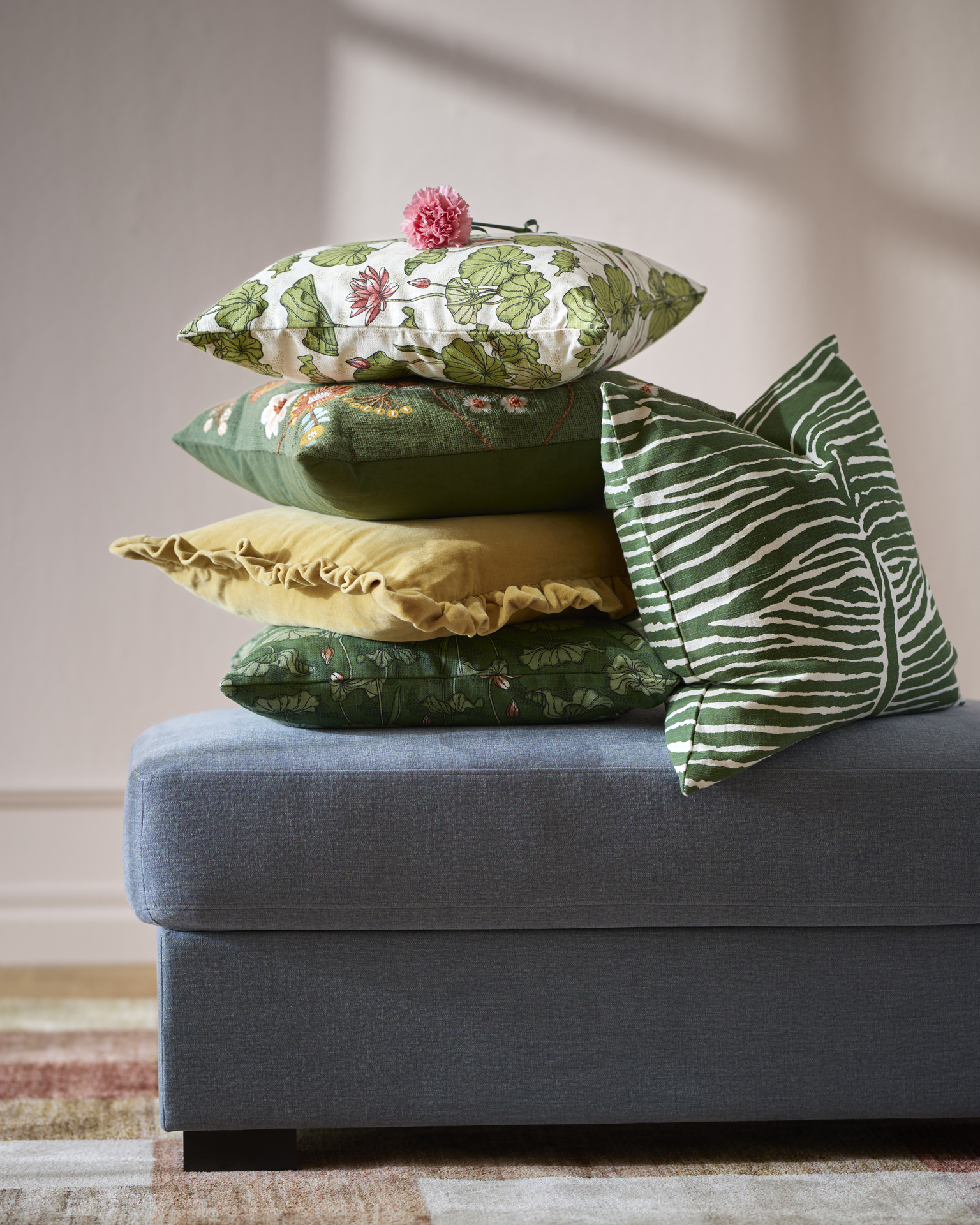 Hög med prydnadskuddar i olika våriga färger ligger på en fotpall i blått. 