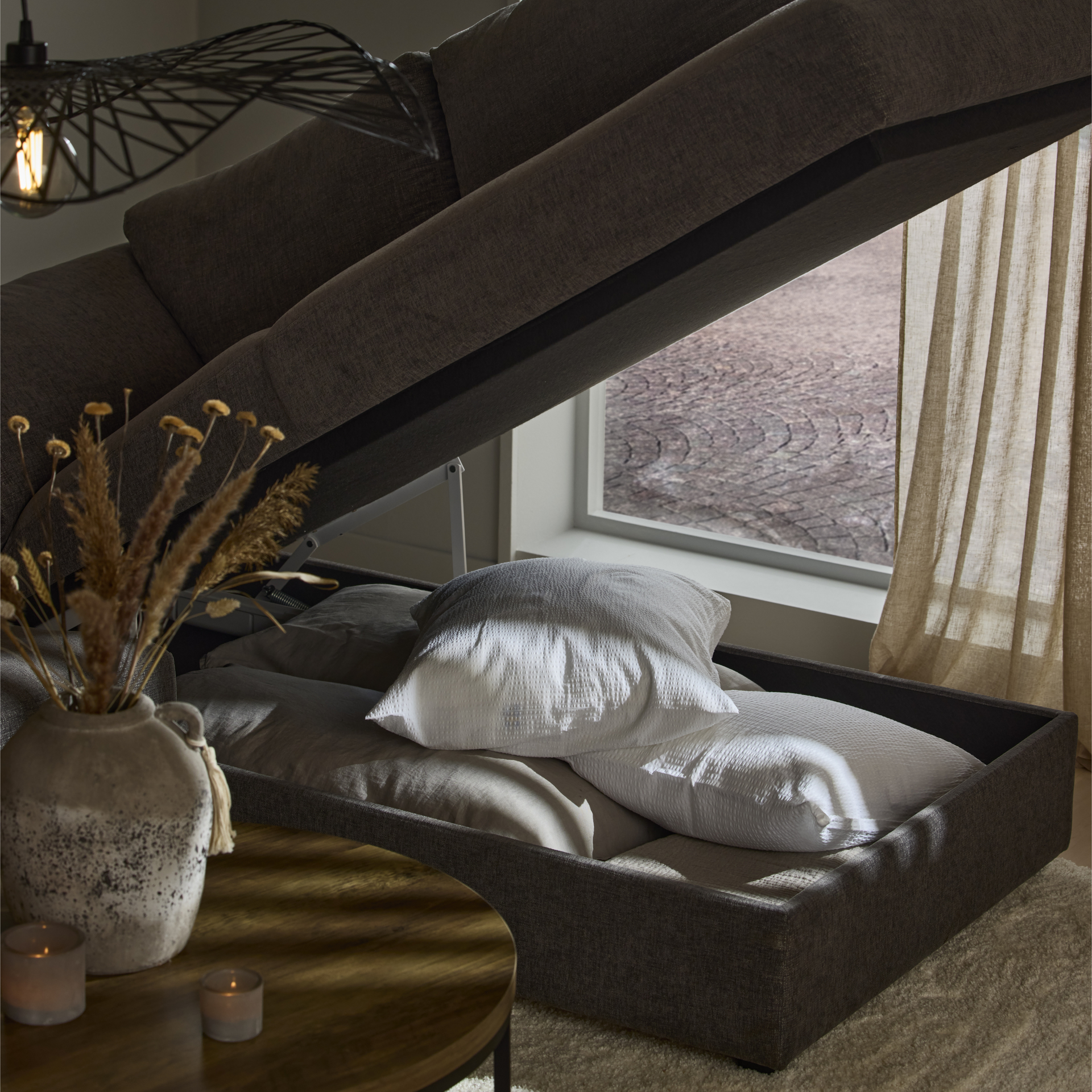 Under divanen på en grå bäddsoffa finns förvaring för kuddar och täcken