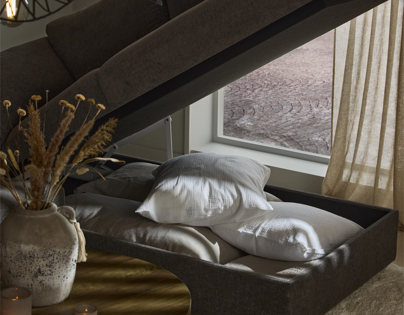 Under divanen på en grå bäddsoffa finns förvaring för kuddar och täcken