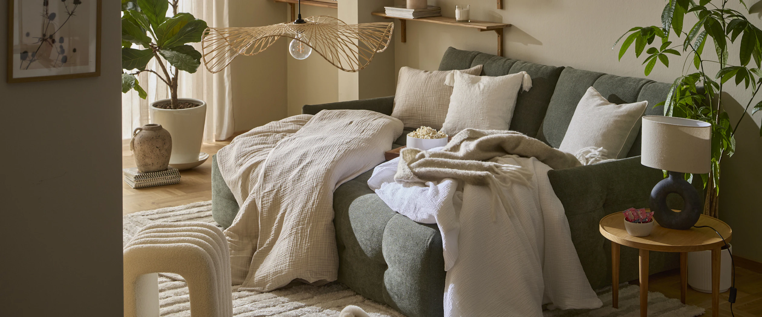 I en grön bäddsoffa ligger fluffiga täcken och kuddar