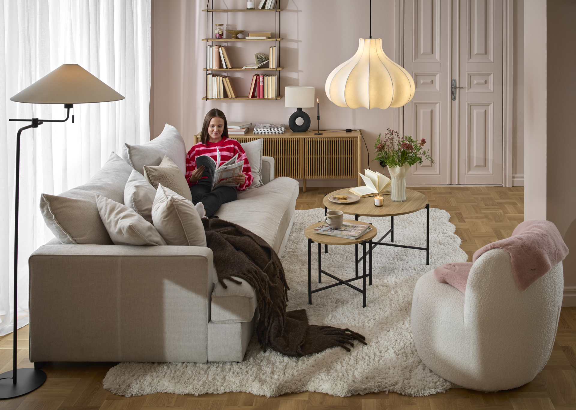 I en vit, djup soffa sitter en kvinna i rosa tröja och läser 