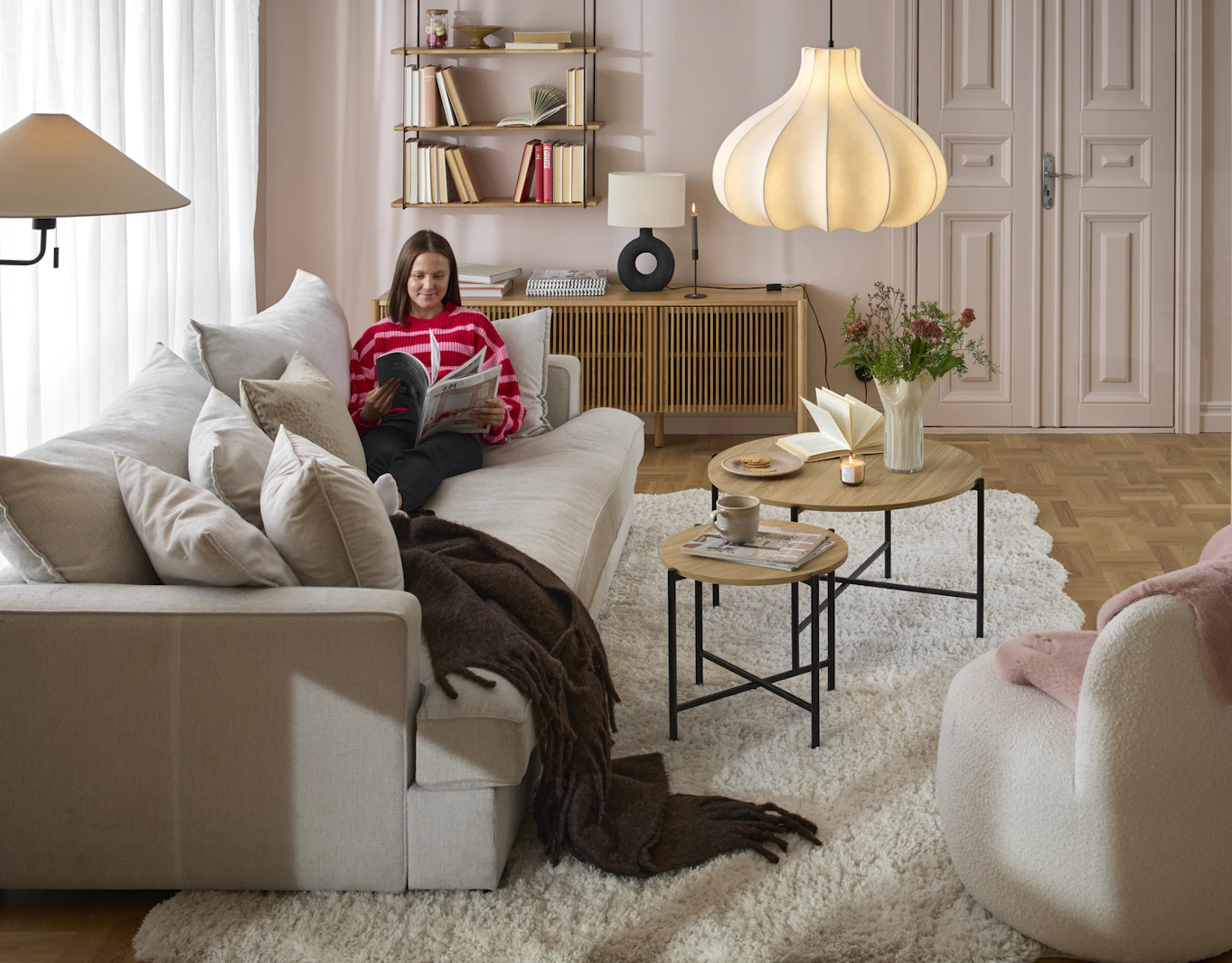 I en vit, djup soffa sitter en kvinna i rosa tröja och läser