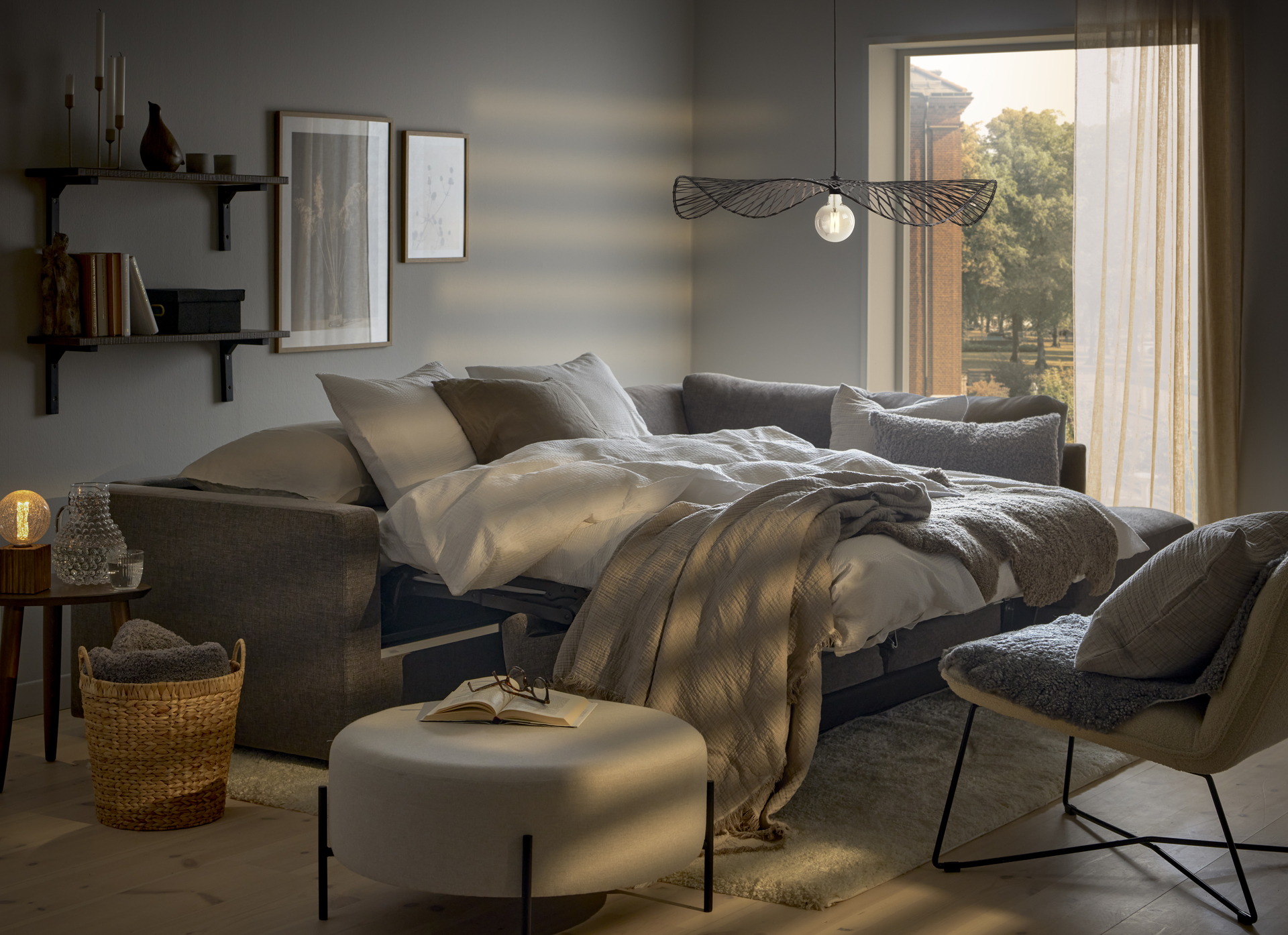 I ett vitt rum står en grå bäddsoffa utbäddad med fluffiga täcken och kuddar