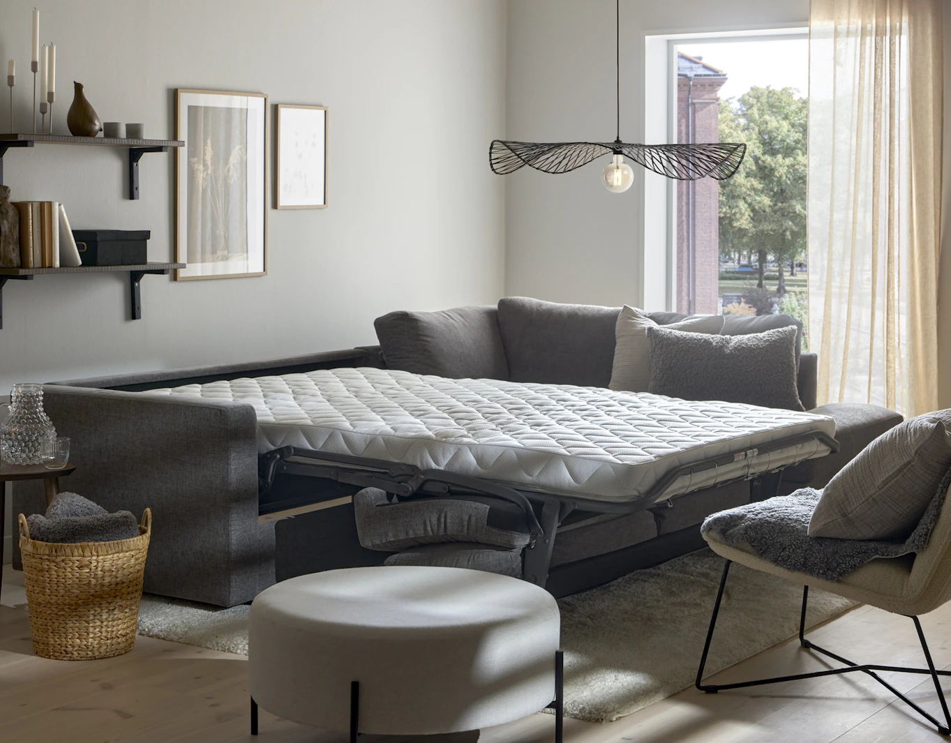I ett vitt rum står en grå bäddsoffa med madrass utbäddad