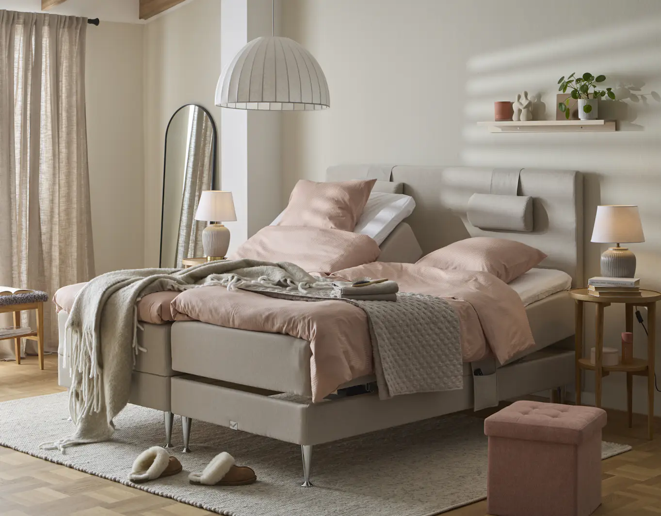 I ett ljust sovrum står en grå ställbar dubbelsäng med rosa sängkläder.