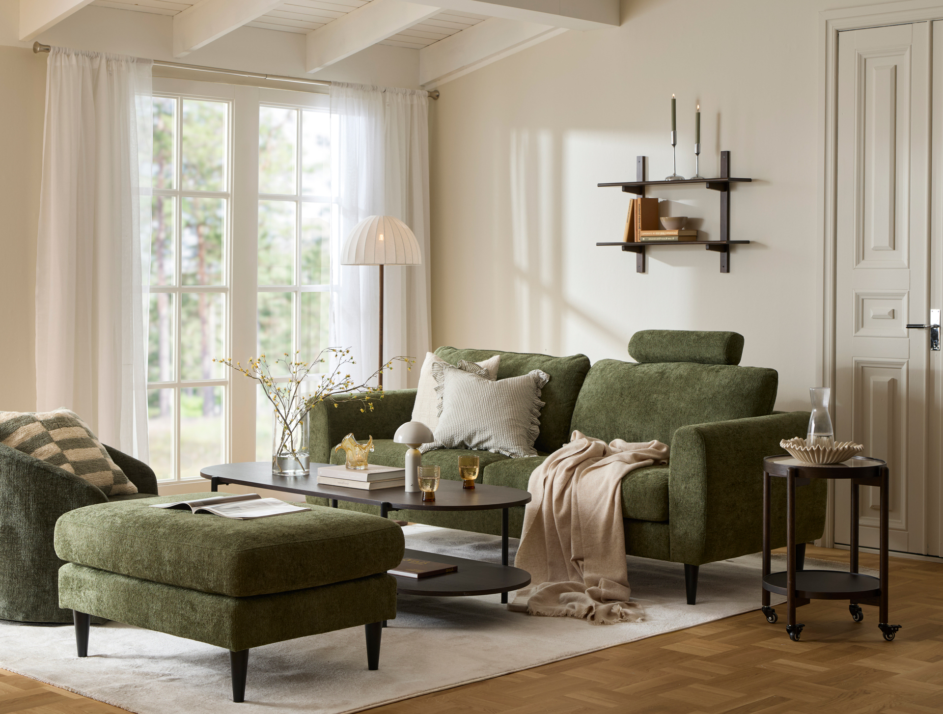 I ett ljust vardagsrum står en grön soffa vid ett soffbord i mörkt trä. Intill står en grön fotpall och en grön fåtölj