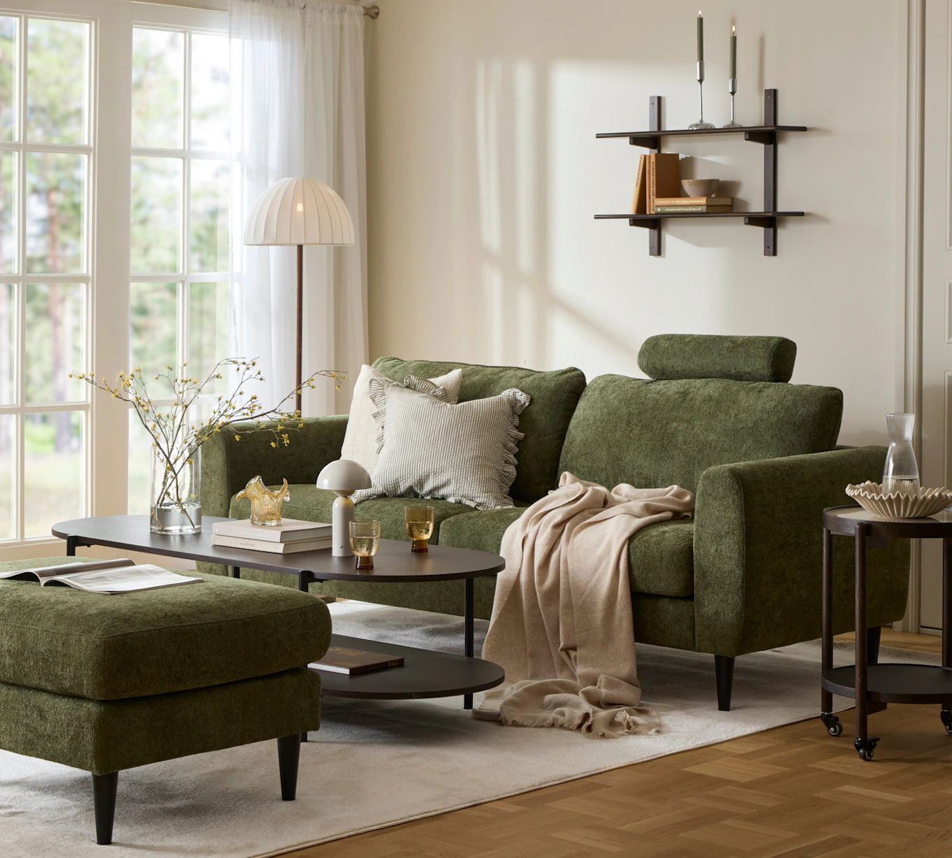 I ett ljust vardagsrum står en grön soffa vid ett soffbord i mörkt trä. Intill står en grön fotpall och en grön fåtölj