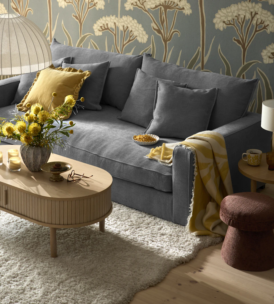 en blå soffa står i ett vardagsrum på en vit matta med vågiga kanter. Framför står ett rektangulärt soffbord med rundade kanter.