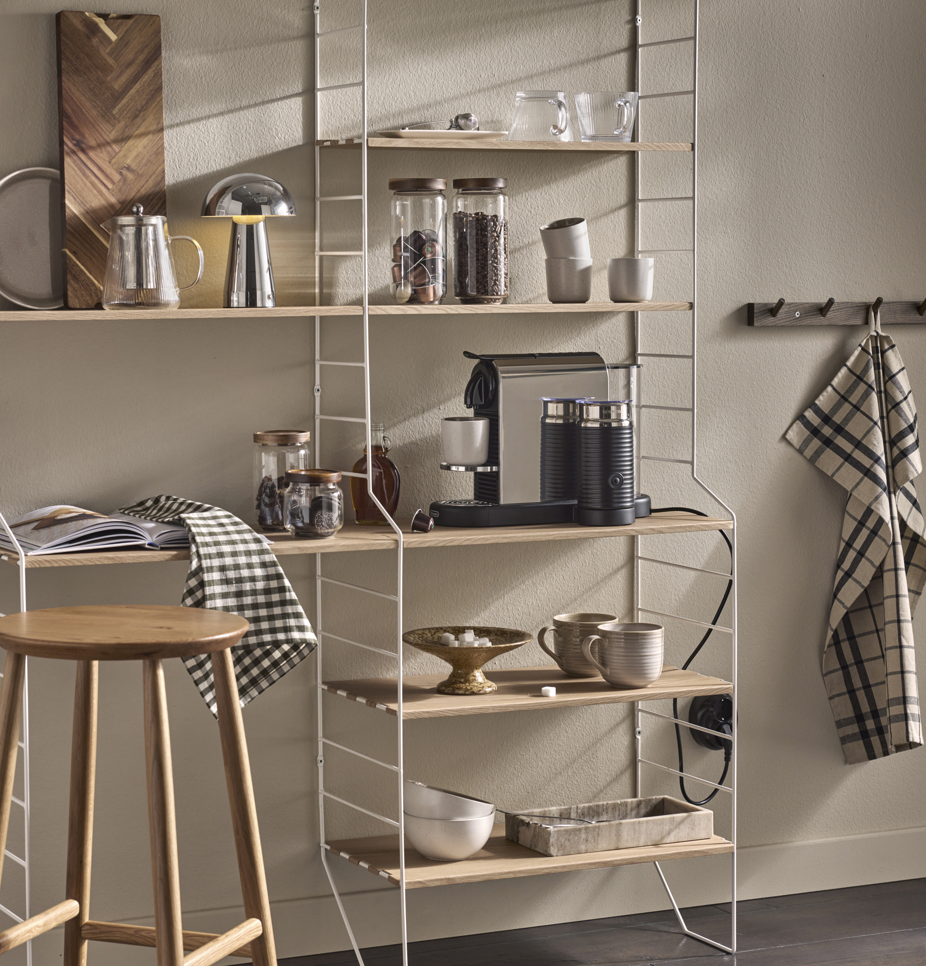 I en kökshylla i vitt och ljust trä står en kaffemaskin och muggar