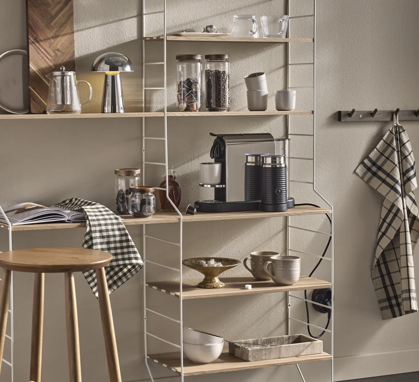 I en kökshylla i vitt och ljust trä står en kaffemaskin och muggar