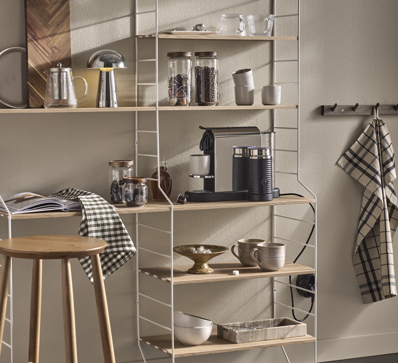 I en kökshylla i vitt och ljust trä står en kaffemaskin och muggar