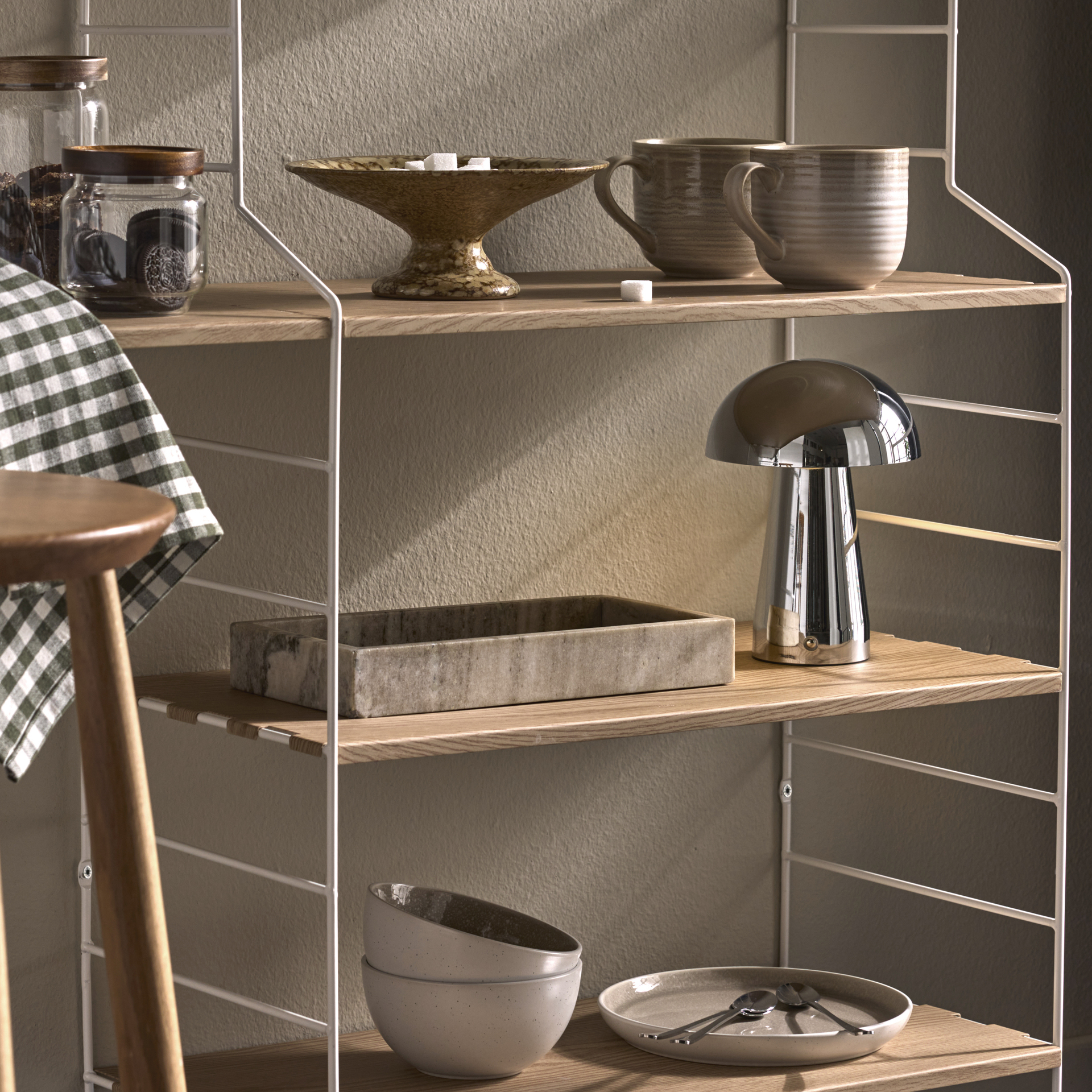 I en kökshylla i vitt och ljust trä står en kaffemaskin och muggar