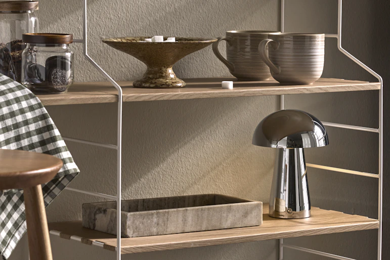 I en kökshylla i vitt och ljust trä står en kaffemaskin och muggar