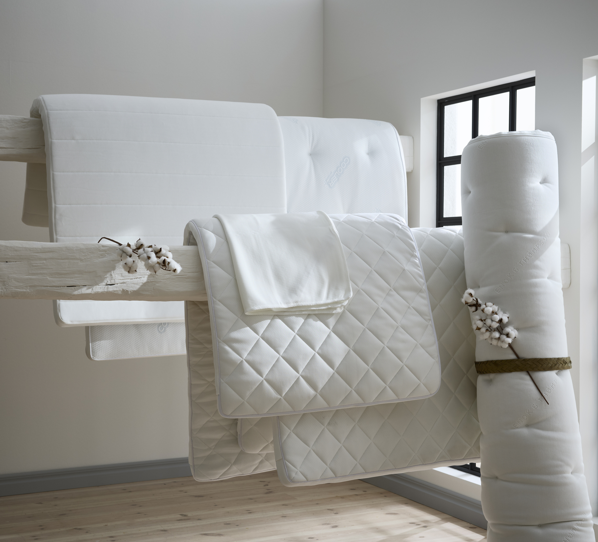 I ett vitt rum hänger bäddmadrasser och madrasskydd på en bjälke