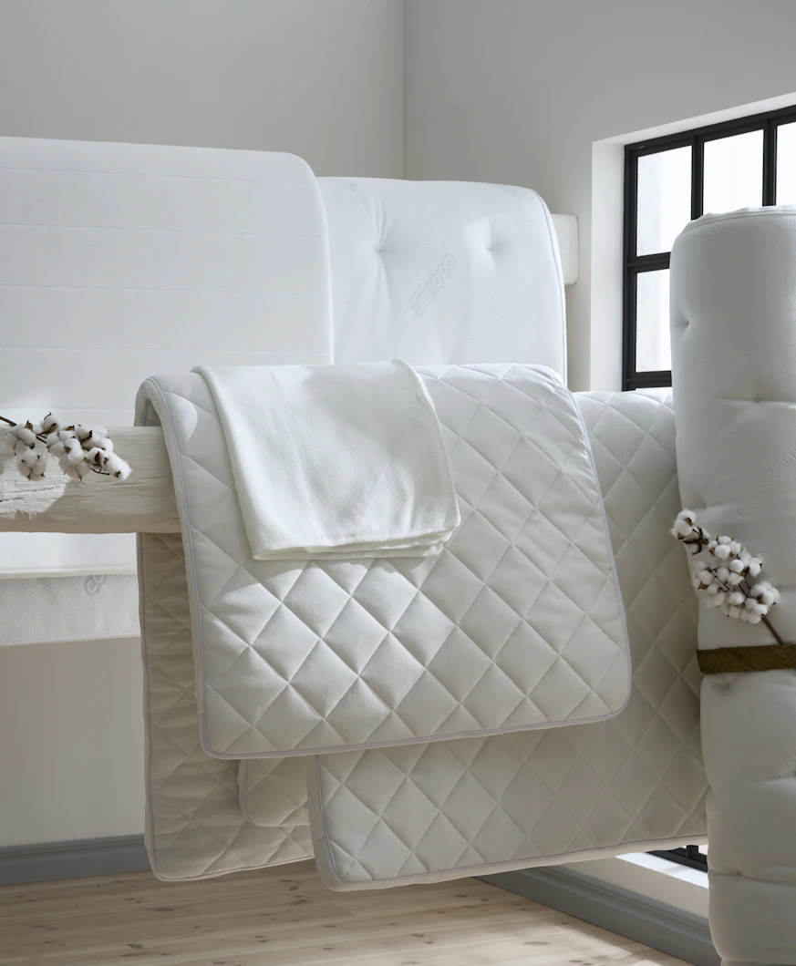 I ett vitt rum hänger bäddmadrasser och madrasskydd på en bjälke