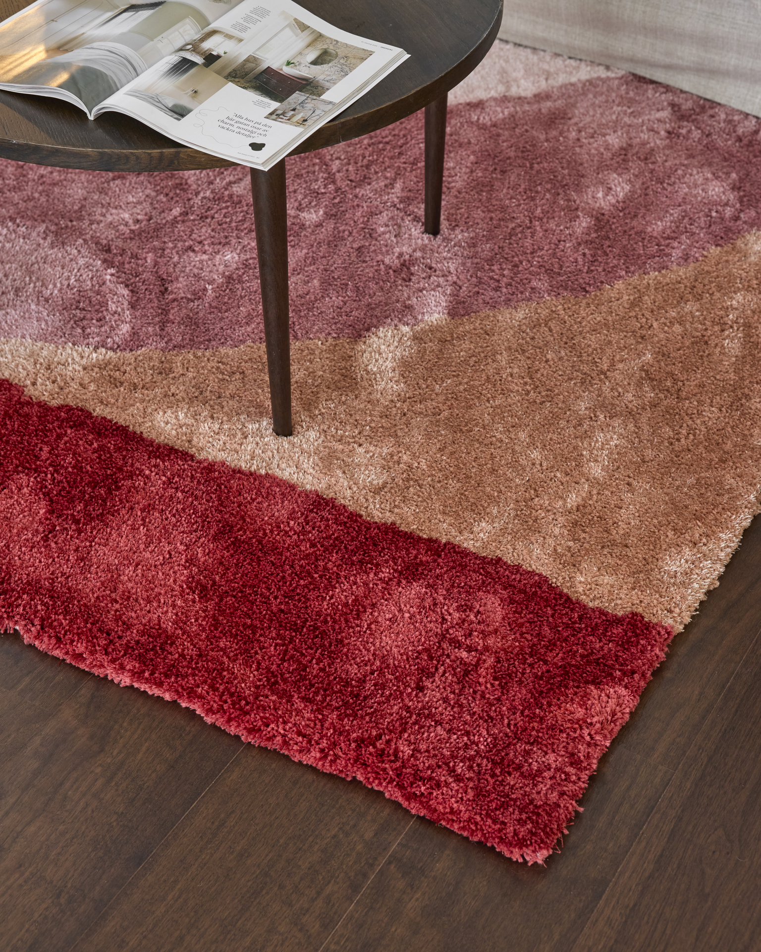 Ett soffbord i mörkt trä står på en färgglad ryamatta i rött, orange och rosa