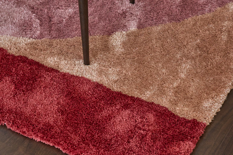 Ett soffbord i mörkt trä står på en färgglad ryamatta i rött, orange och rosa