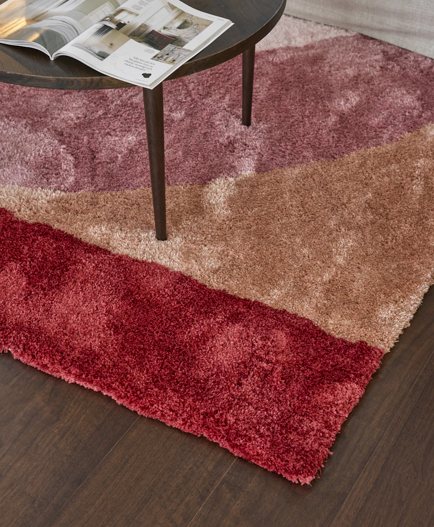 Ett soffbord i mörkt trä står på en färgglad ryamatta i rött, orange och rosa