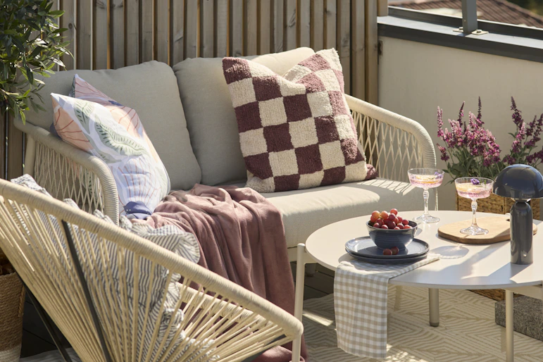 På en balkong står en beige utesoffa, en fåtölj och ett bord