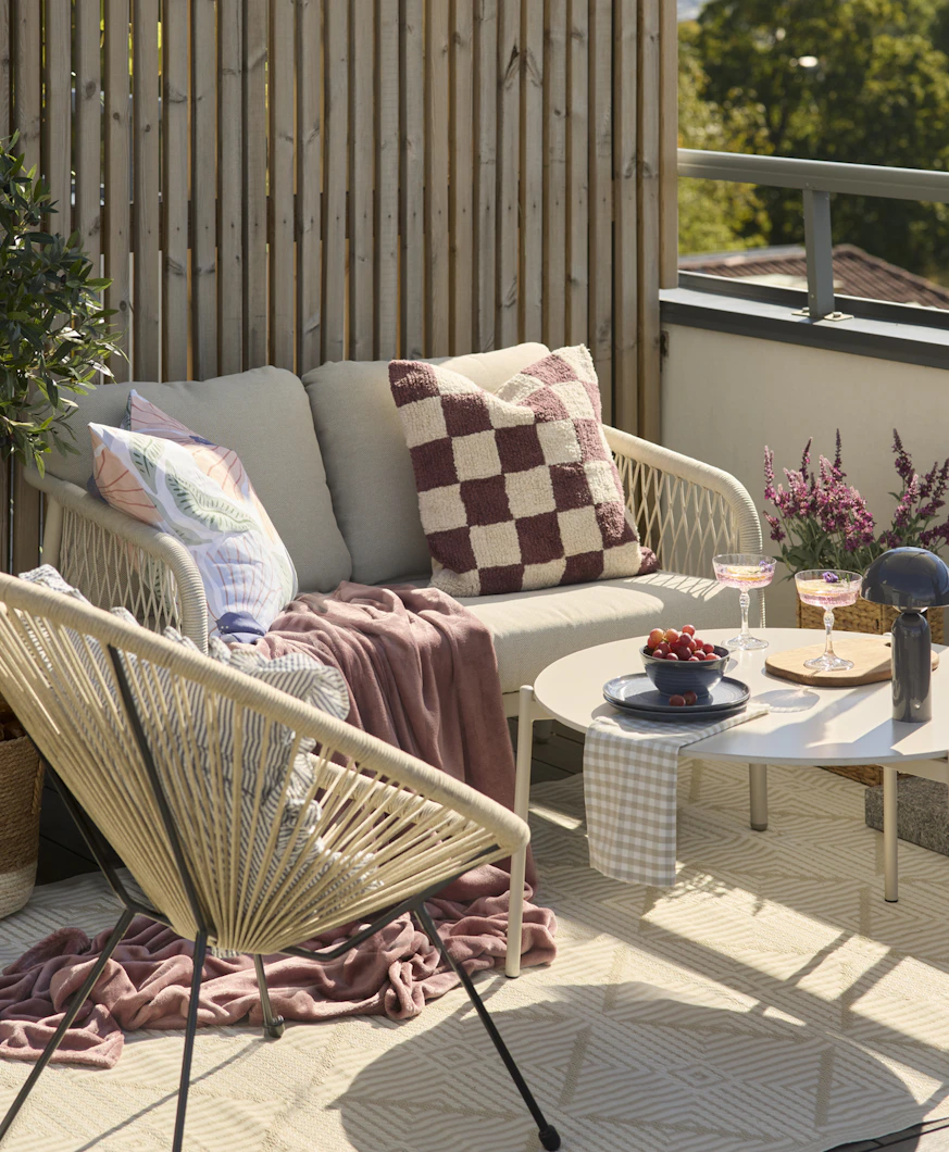 På en balkong står en beige utesoffa, en fåtölj och ett bord