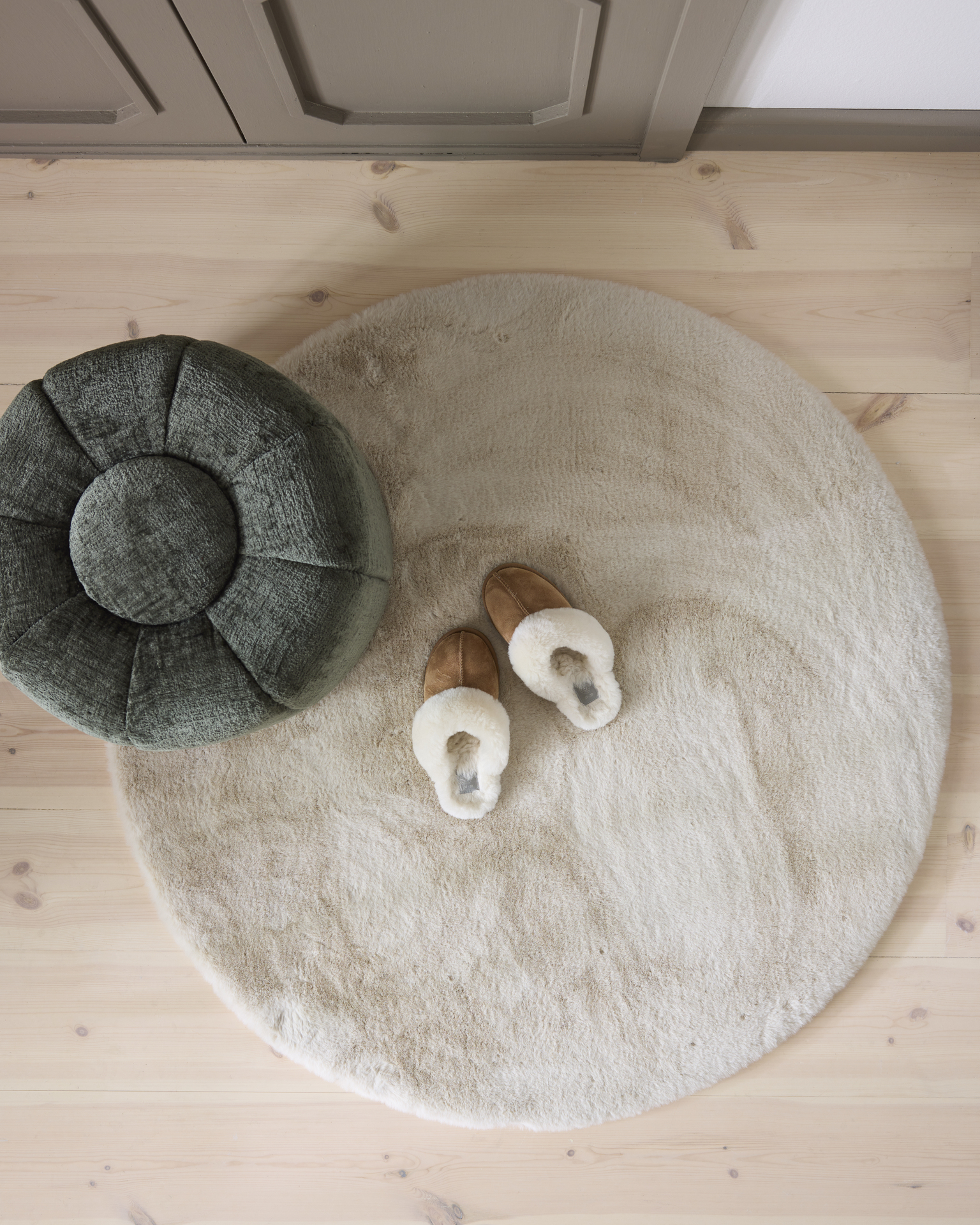 På en vit rund matta står en grön fotpall och ett par bruna tofflor.