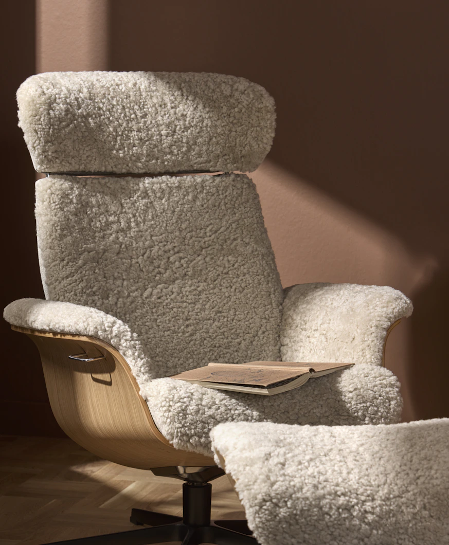 I ett terracotta rött rum står en vit fårskinnsfåtölj med detaljer i ljust trä