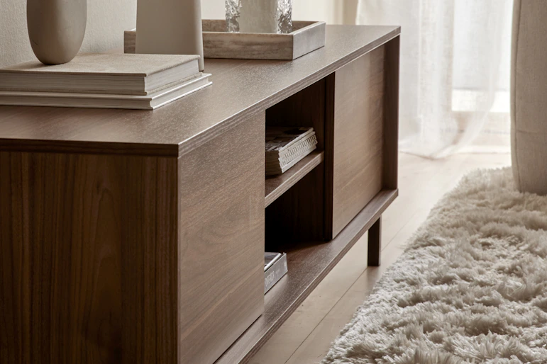 I ett ljust rum står en TV-bänk i valnöt dekorerad med vackra ting