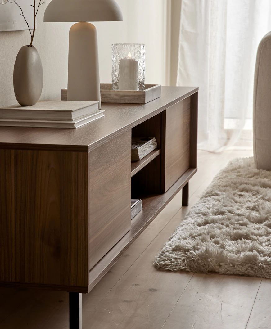 I ett ljust rum står en TV-bänk i valnöt dekorerad med vackra ting