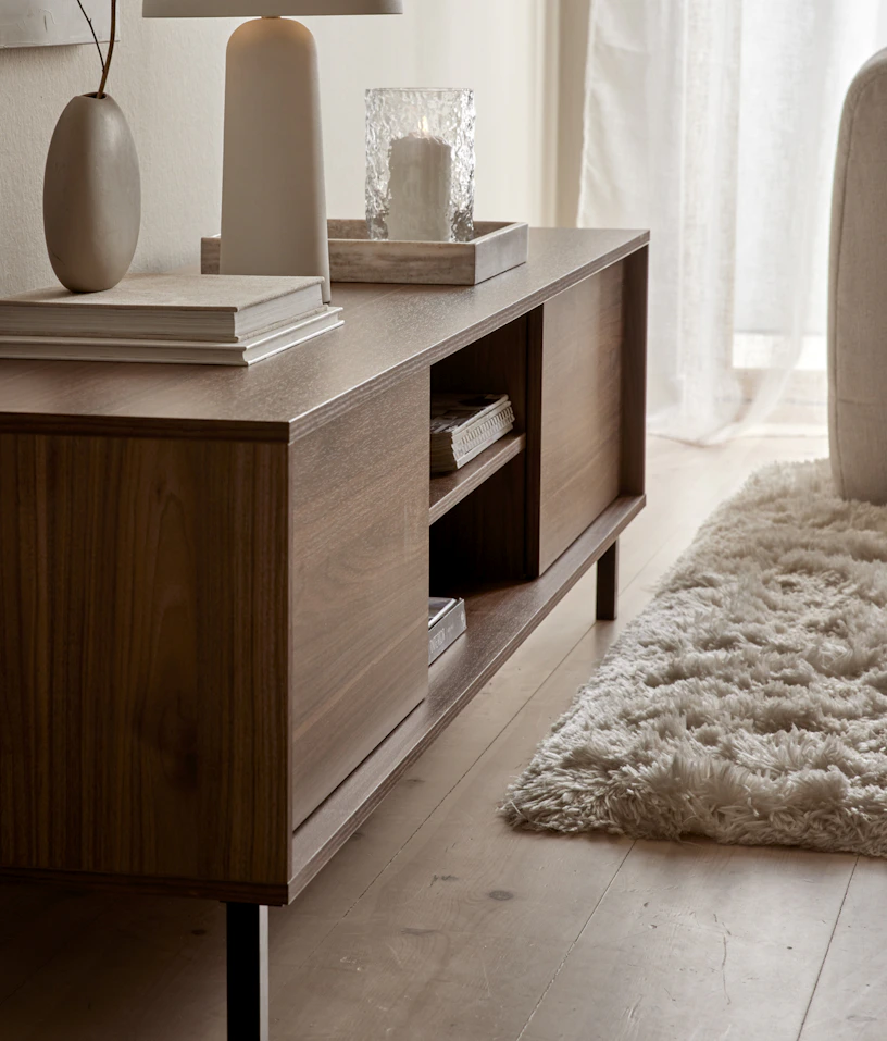 I ett ljust rum står en TV-bänk i valnöt dekorerad med vackra ting