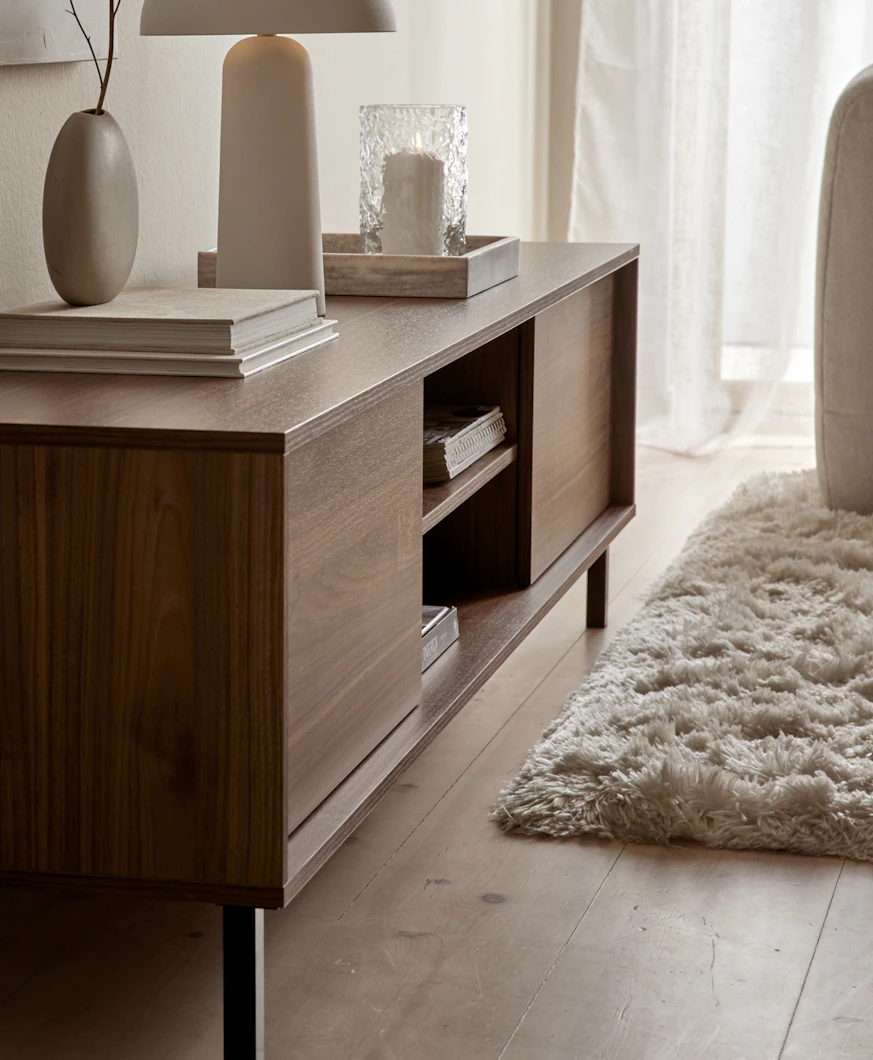 I ett ljust rum står en TV-bänk i valnöt dekorerad med vackra ting