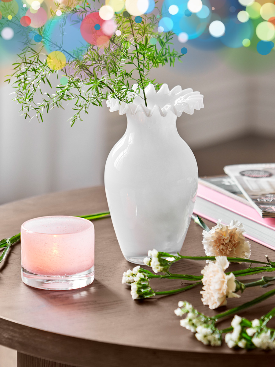 en vit vas med några kvistar, en rosa ljuslykta och blommor är placerade på ett brunt bord