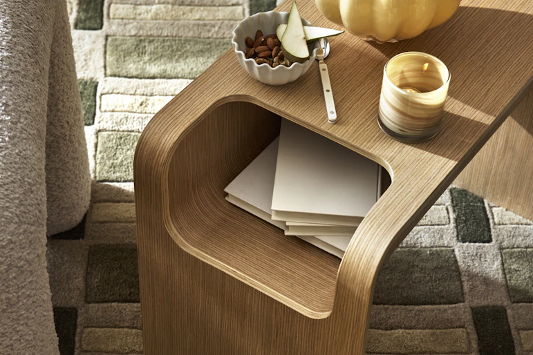 På en grön, mönstrad matta står ett sidobord i ek dekorerad med en gul vas och en ljuslykta