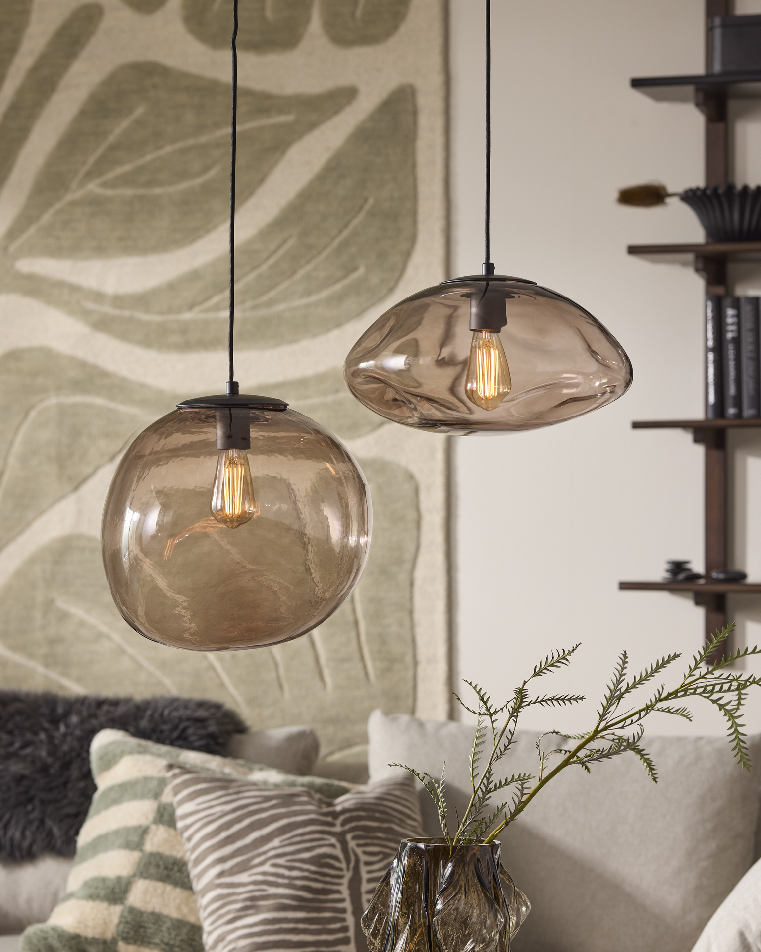 I ett vardagsrum hänger två taklampor i rökfärgad glas med organisk form
