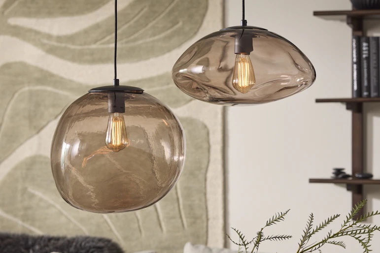 I ett vardagsrum hänger två taklampor i rökfärgad glas med organisk form