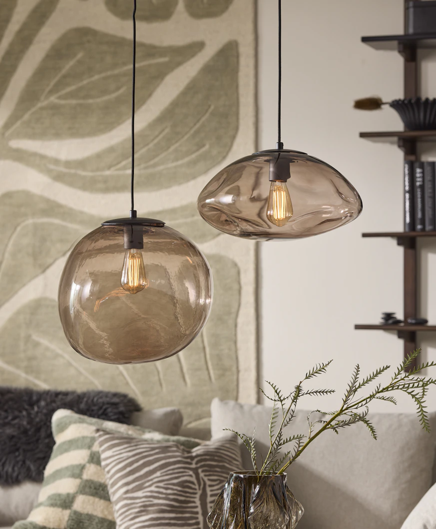 I ett vardagsrum hänger två taklampor i rökfärgad glas med organisk form