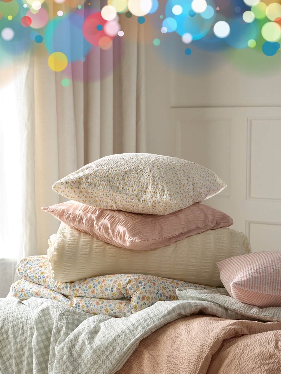 kuddar och täcken med olika påslakan och örngott i ljusa färger ligger i en hög på en säng