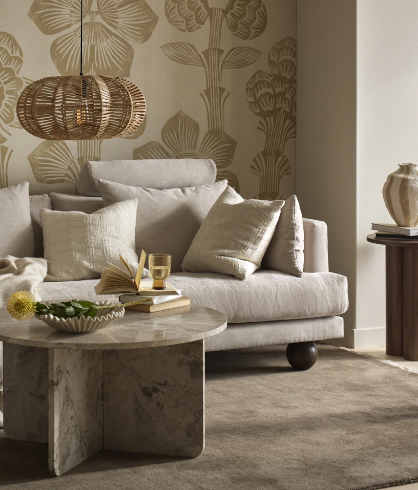 I ett vardagsrum står en beige soffa med runda ben i mörkt trä