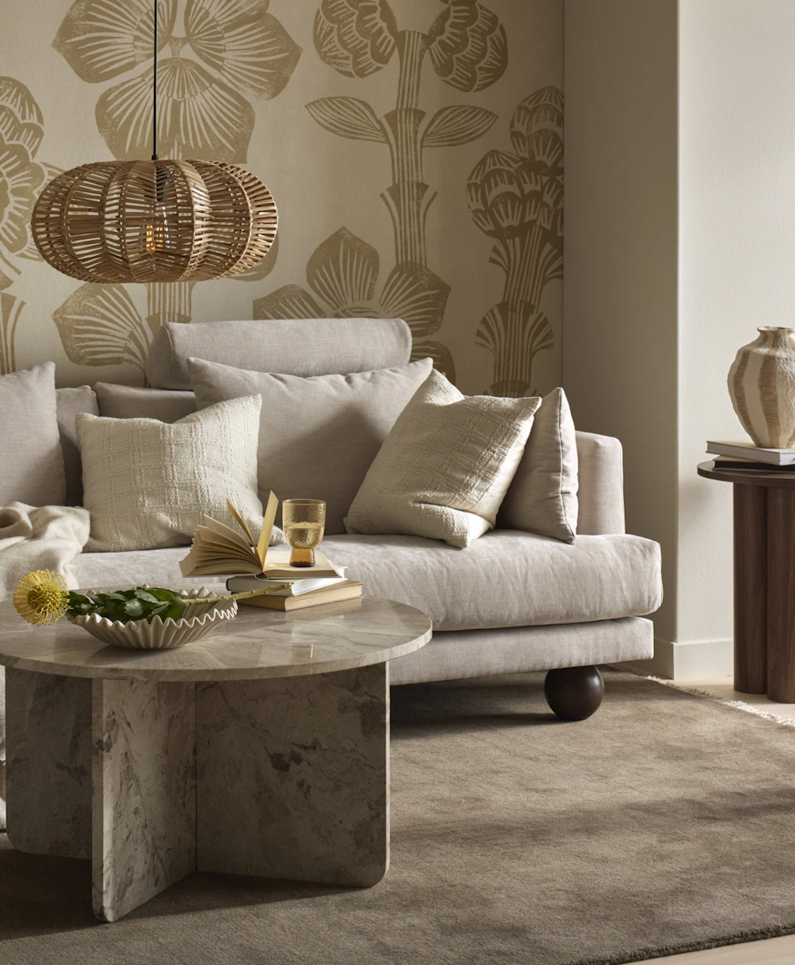 I ett vardagsrum står en beige soffa med runda ben i mörkt trä