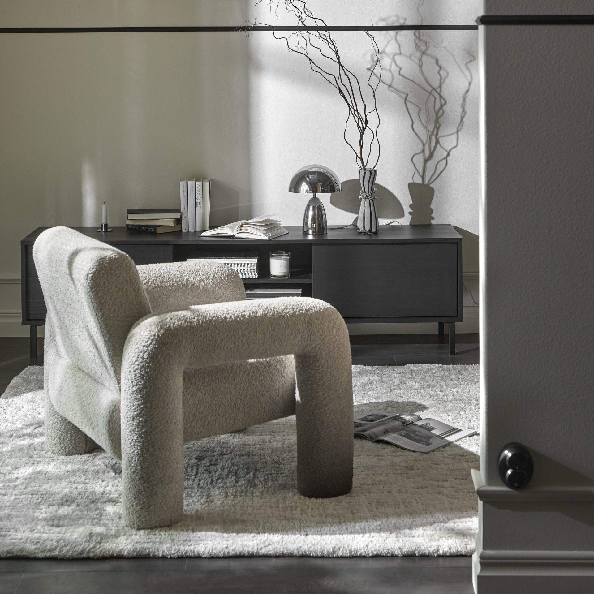 En vit fåtölj i modern design med rundade former står framför en tv-bänk i mörkt trä