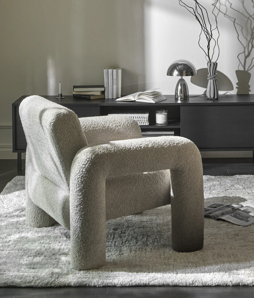 En vit fåtölj i modern design med rundade former står framför en tv-bänk i mörkt trä