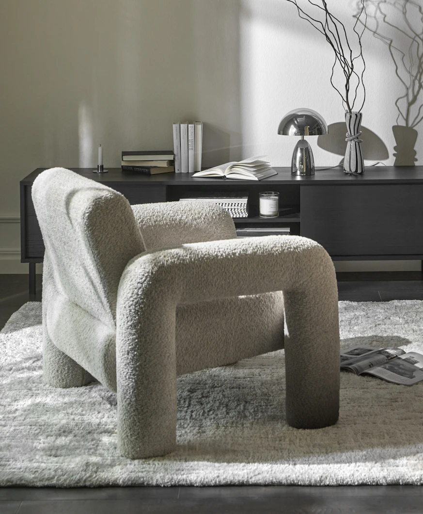 En vit fåtölj i modern design med rundade former står framför en tv-bänk i mörkt trä