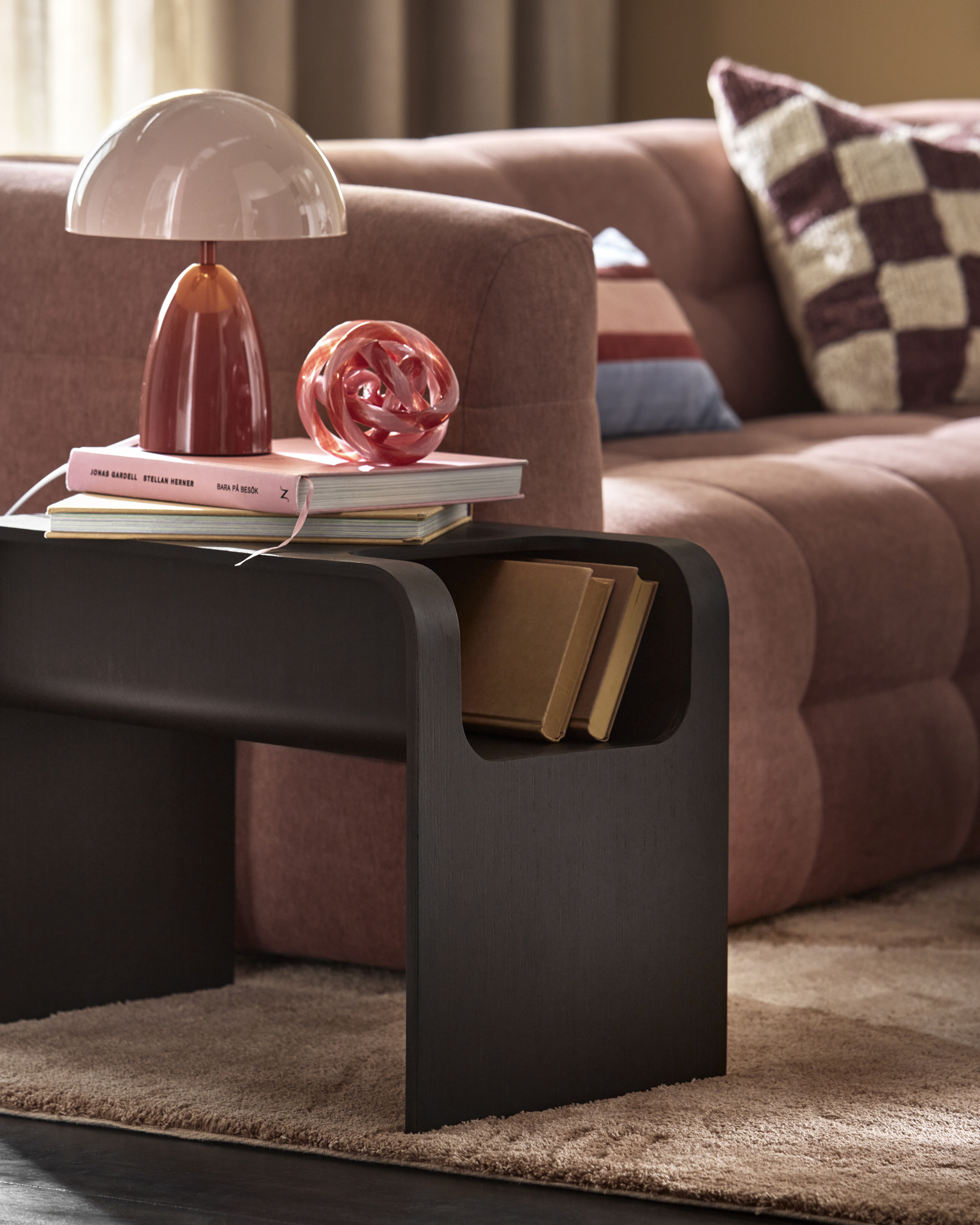 Bredvid en rosa soffa står ett sidobord i mörkt trä