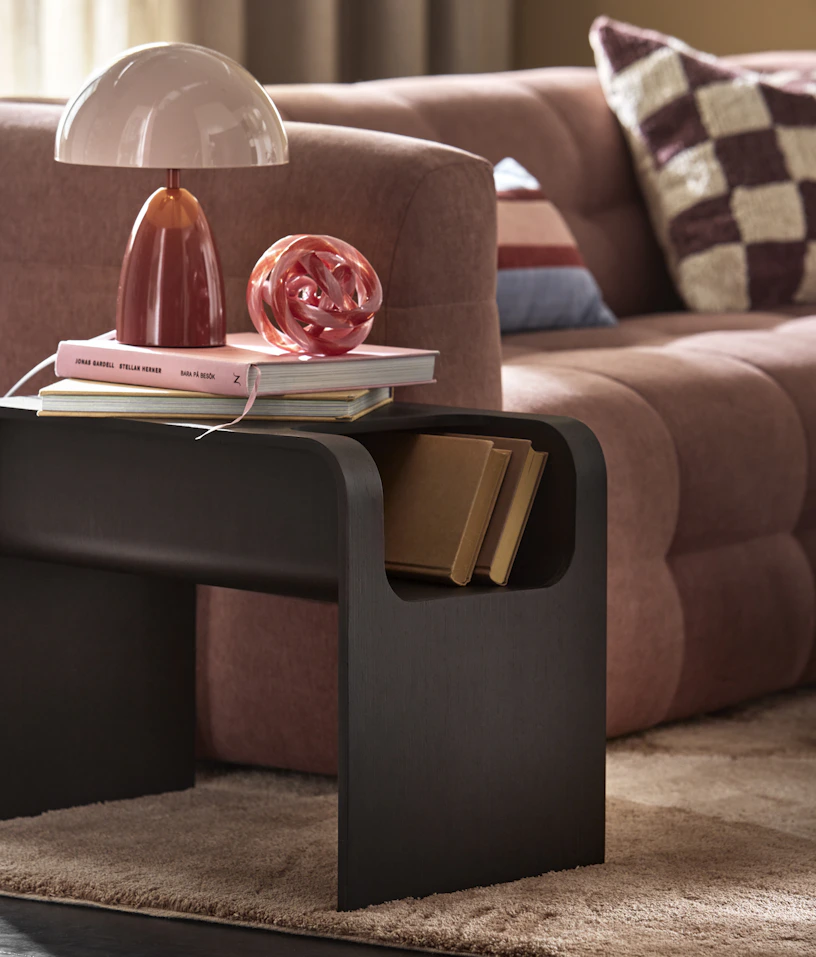 Bredvid en rosa soffa står ett sidobord i mörkt trä